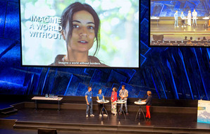 Interviewsituation auf der Bühne, auf der Leinwand ein Filmbeitrag