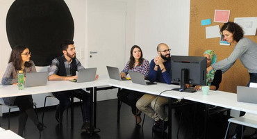 Lehrerin erklärt einer Gruppe von erwachsenen diversen Schülerinnen und Schülern etwas