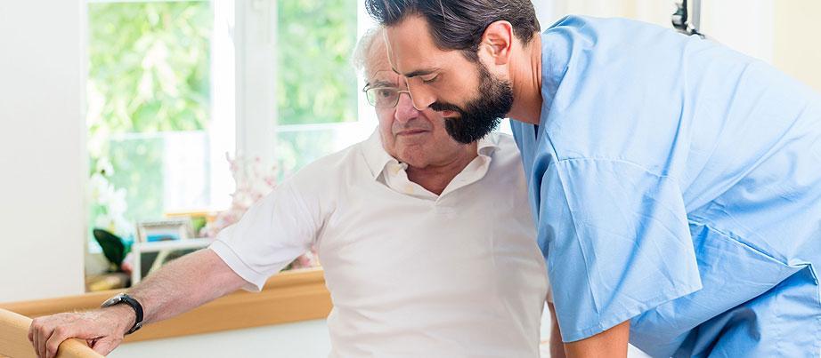 Junger Pfleger hilft einem pflegebedürftigen Senior aus dem Bett