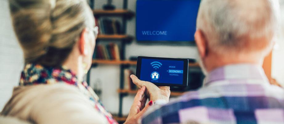 Seniorin und Senior gemeinsam auf dem Sofa mit einer Fernbedienung für ein intelligentes Zuhause