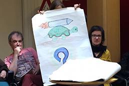 Zwei Frauen halten ein Bild hoch, auf dem eine Schildkröte gemalt ist.