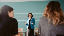 Lehrerin an einer Tafel mit Blick zu Schülerinnen 