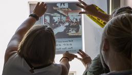 Menschen sehen sich ein Plakat mit Bild an, welches an ein Fenster gehalten wird