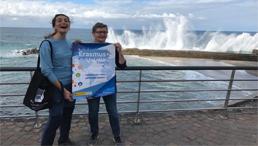 Zwei Frauen halten ein Tuch am Meer stehend hoch